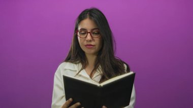 Stüdyo ortamında pembe duvarları olan bir kitabı açık tutarken genç kadın işaret ediyor; davet.
