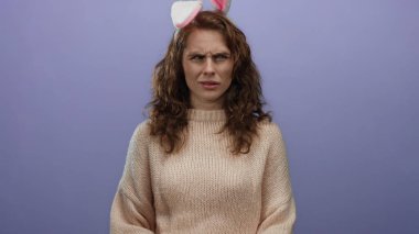 Kıvırcık saçlı, tavşan kulaklı bir kadın, izole edilmiş mor bir arka plana karşı şaşkın, rahat bir kazak giymiş, tuhaf bir tatil belirsizliğini yakalıyor..