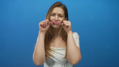 Beyaz omuzlu genç bir kadın dudaklarını büzüyor ve mavi stüdyo setinde yüzüne yumruk atıyor. Üzüntü..