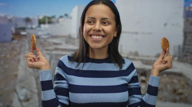 Yüzünün yanındaki kurabiyeleri tutan genç İspanyol kadın şantiyeye gülüyor. Neşeli ve neşeli çizgili bir süveter giyiyor ve enerjik bir şekilde yakalanmış..