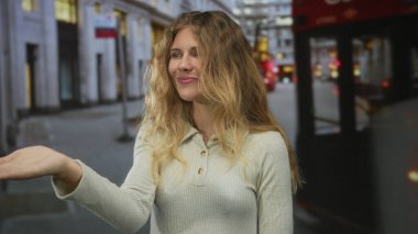 Bir kadın, Londra 'da bir arka planda, otobüsün yanında gülümseyen bir sarışınla elini uzatıyor..