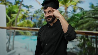 Siyah şef üniformalı bir adam arka planda palmiye ağaçları ve otelle dışarıda duruyor. Kafasını göstererek düşünceli bir ifade sergiliyor. Mutfak yaratıcılığını ima ediyor..