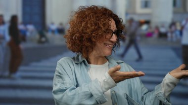 Kalabalık bir caddede el kol hareketi yapan bir kadın, arka planda insanların olduğu bir şehir sahnesini çekiyor..