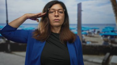 Mavi ceketli İspanyol kadın, güneşli sahil plajında sağ eliyle selam veriyor. Görev disiplinine saygı gösterin..