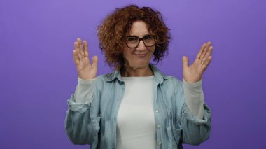 Orta yaşlı İspanyol bir kadın, elleri mor bir duvarın önünde, gözlük ve kot gömlek giyer ve büyük beden bir konsept taşır..