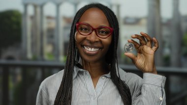 Bir kadın açık şehir ortamında elinde ethereum sikke tutarken gülümsüyor kripto para birimi ilgisini ve modern finansal eğilimleri gösteriyor.