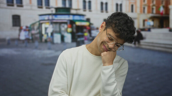 Мужчина в белом свитере и круглых очках, лежащих подбородок на руке на оживленной улице города; самоанализ.