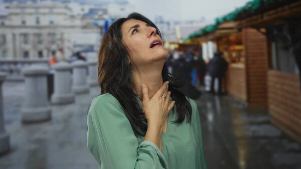 Латиноамериканка средних лет щекочет нос возле сувенирного ларька на переполненном городском рынке; неприятный дискомфорт.