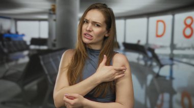 Havaalanı terminalinin sol tarafında sol omuz tutan kadın kolsuz gri bluz giyiyor..