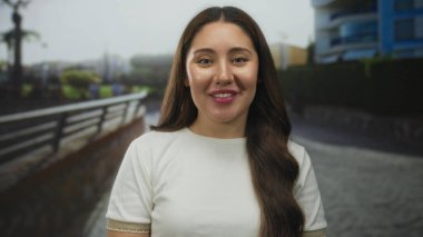 Caddede beyaz bir tişört içinde görünen dudakları olan Latin kökenli genç bir kadın konuşuyor; özgüven bağlantısı özgünlüğü.