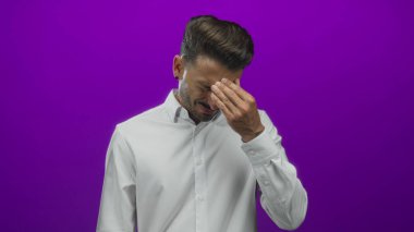 Beyaz gömlek giyen genç adam stüdyoda gözleri mor arkaplan ile kaplıyor; stres.