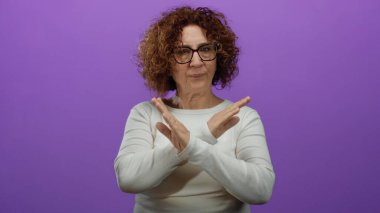 Orta yaşlı İspanyol bir kadın, beyaz bir bluzla, izole edilmiş mor bir arka plana karşı duruyor..