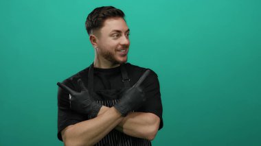 Sakallı ve eldivenli genç garson her iki yönü de parlak yeşil bir arka plana işaret ediyor. Önlük takıyor ve kendine güveni tam..