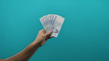 Güney Kore 'yi elinde tutan adam mavi arka plan duvarına karşı banknotlar kazanarak para ve mali işlem temaları minimalist bir ortamda vurgulandı.