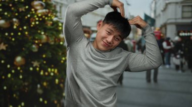 Gri tişörtlü, enerjik bir şekilde gülümseyen genç adam, neşeli şehir sokaklarında bayram kutlamaları için süslenmiş..