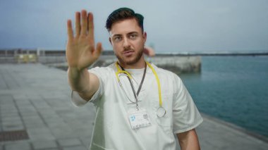 Steteskoplu beyaz önlüklü genç sakallı doktor deniz kenarında okyanus manzaralı gezinti yapmaz.