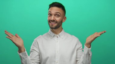 Kolları havada gülümseyen genç İspanyol bir adam canlı yeşil arka planda beyaz gömlekli, kendinden emin ve cana yakın görünüyor.