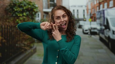 Şehirli şehir sokaklarında hashtag sembolü taşıyan bir kadın, yeşil kazak giyiyor, enerjik bir şekilde gülümsüyor, sosyal medyayı ve yaşam tarzını ön plana çıkarıyor..