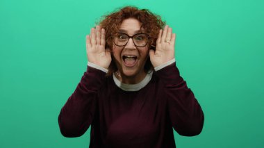 Gülümseyen ve neşeli bir şekilde yüzünü kapatan bir kadın, canlı yeşil bir arka plana karşı mutluluğu gözler önüne seriyor, anlamlı neşesini ve enerjisini vurguluyor..