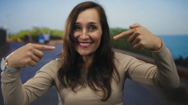 Genç İspanyol kadın deniz kenarındaki gezinti alanında kendini işaret ediyor; kendine güven gururu.