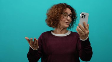 Mavi izole edilmiş bir arka planı olan akıllı telefondan gülümseyen bir kadın orta yaşlı İspanyol kimliğini sergiliyor ve iletişim teknolojisini ön plana çıkarıyor..