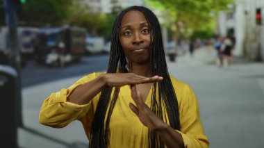 Şehir sokaklarında el kol hareketi yapan bir kadın açık şehir ortamında iletişim kuruyor. Sarı elbiseli ve uzun saçlı..