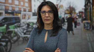 İspanyol kadın gözlük takıyor ve mavi kazak gün ortasında şehir caddesinde kol kola giriyor; reddedilme.