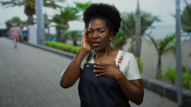 Önlük giymiş bir kadın sahilde palmiye ağaçlarıyla dikiliyor. Sahilde yürürken ve konuşurken, sakin bir okyanus manzarasıyla duyguları iletiyor..