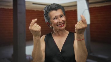 Kapalı bir şantiyede, gri saçlı yaşlı bir kadın, siyah bir elbise ve kırmızı bir bilezik takıyor, neşeli bir ifadeyle, zenginlik ve zenginliği simgeliyor..