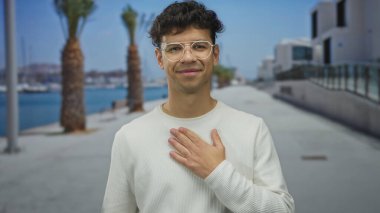 Deniz kenarındaki güvertede mavi denizin yanında palmiye ağaçları olan beyaz süveter giyen bir adam. Acı..