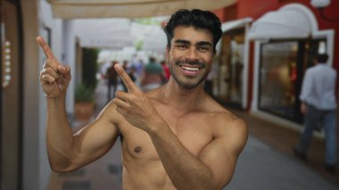 Çıplak göğüslü bir adam sabah güneşinin altında geniş bir gülümseme ve meşgul şehir caddesinde parmak işareti; güven.