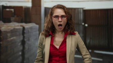 İnşaat alanında gözlük takan ve spor ceket giyen bir kadın, arka plandaki yapı malzemeleriyle farklı duygular ifade ediyor..