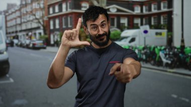 Sokak ortasında İspanyol bir adam şehir binalarının önünde el kol hareketleri yapıyor ve park halindeki araçlar samimi bir ifade ve duygu anı yakalıyor..