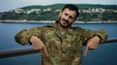 Sakallı, askeri üniformalı İspanyol bir adam okyanus ve arka planda yeşillik olan bir yolcu gemisini işaret ediyor..