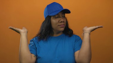 Mavi şapkalı ve gömlekli kadın, parlak turuncu stüdyoda avuçlarını hafifçe eğerek havada tutuyor..
