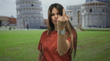 Kırmızı gömlekli genç bir kadın Avrupa 'nın manzaralı bir simgesi önünde orta parmağıyla jest yapıyor. Kırmızı tonlu arka plana karşı güneşli ve açık havada isyankar bir tavır sergiliyor..