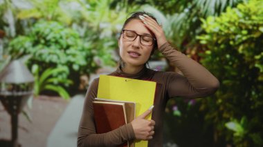 Parkta elinde kitaplarla gezen genç bir kadın yeşil yeşilliklerin arasında stresli bir görünüm serinletici, huzurlu bir ortam ve dinlendirici doğal bir geri çekilme.