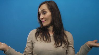 Mavi arka plan duvarına karşı belirsizlikle omuz silken bir kadın gündelik ve karışık bir ifade sergiliyor..