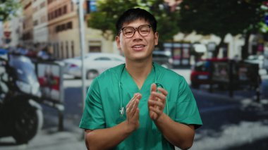 Tıbbi önlüklü genç adam hareketli bir şehir caddesinde neşeyle gülüyor ve alkışlıyor, canlı bir şehir ortamında mutluluk ve pozitifliği yansıtıyor..