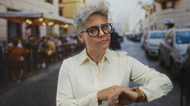 Beyaz tişörtlü, siyah gözlüklü bir kadın restoranın teras sokağında izlemek için işaret ediyor. Sabırsızlık..