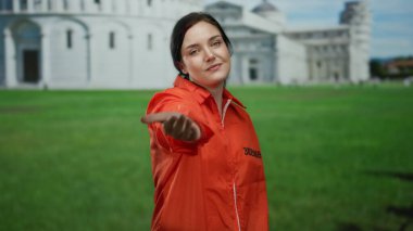 Turuncu hapishane tulumu giymiş bir kadın İtalya 'daki Pisa Kulesi' nin önünde el kamerasına uzanıyor. Hapishaneyi ikonik mimariyle harmanlayan eşsiz bir sahneyi yakalıyor..