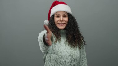 Kırmızı Noel Baba şapkalı ve rahat kazaklı bir kadın izole edilmiş gri arka plan duvarına uzanıyor.