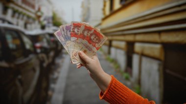 Kentsel bir sokakta Kolombiya pezosu tutan kadın, canlı bir şehir ortamında para ile iş potansiyelini sergiliyor, ekonomik temaları ve açık hava aktivitelerini vurguluyor..