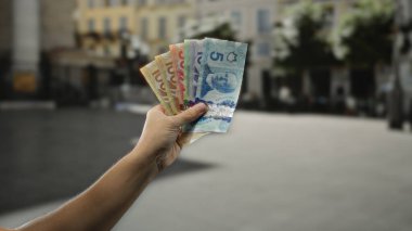 Bir şehir caddesinde renkli Kanada banknotları tutan bir adam, açık hava ortamında para gösteriyor, finansal odak ve uluslararası seyahat vurguluyor.