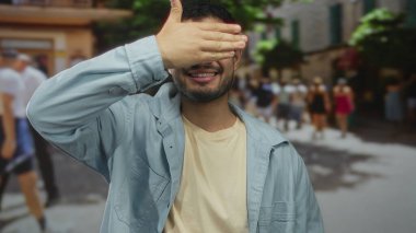 Genç adam gülümserken hareketli sokakta elleri ile gözlerini kapar; gizemli oyun merak mahremiyet.