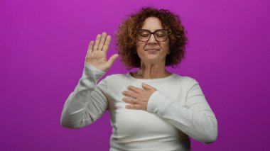 Gözlüklü, eli yürekli orta yaşlı bir kadın canlı pembe duvara karşı yemin ederek yükseldi. Stüdyo ortamında samimiyet ve sadakat gösteriyordu.