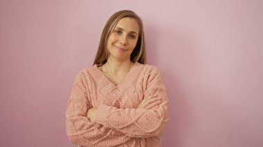 Pembe kolları katlanmış bir kadın soluk pembe arka planda kendine güvenen bir ifade sergiliyor. Kapalı mekanda yalnızlık, sıcak stil profesyonellerin olgunluk kıyafetlerini yumuşakça giyinmelerini sağlıyor.