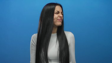 İzole edilmiş mavi arka plan duvarına karşı duygularını ifade eden genç İspanyol kadın, bir dizi yüz ifadeleri ve jestler sergiliyor..