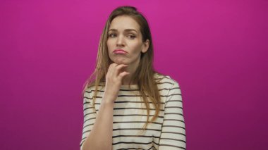 Genç, beyaz bir kadın canlı pembe stüdyo portresiyle yanağına bastırıyor, şüphe yansımasını düşünüyor..