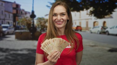 Kırmızı tişörtlü, beyaz bir kadın. Elinde banknotlar var. Yardım derneği cömertliği..